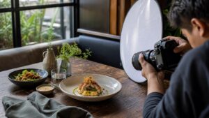 Restaurant table food photography setup with camera, reflector, and plated dish